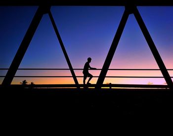 Silhouette boy playing on playground against clear sky during sunset