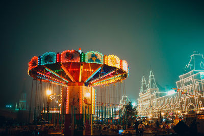 Illuminated amusement park ride against sky at night