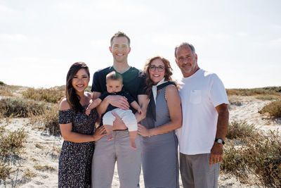 Family of five smiling on beach with sun behind