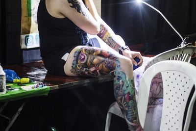 Midsection of man with tattoos on hands and leg sitting on table