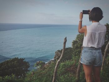 Rear view of boy photographing sea against sky