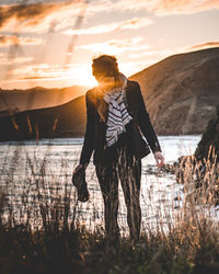 Full length of woman standing by lake against sky during sunset