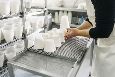 Male chef arranging cheese on table by rack in dairy factory