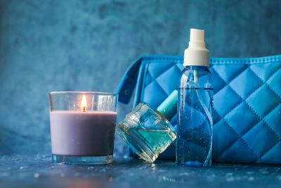 Close-up of small spray bottle with clutch bag and candle on blue table