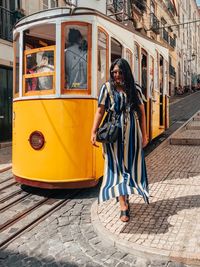 Full length portrait of young woman standing by tram in city