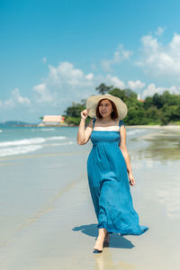 Full length of young woman standing at beach against sky