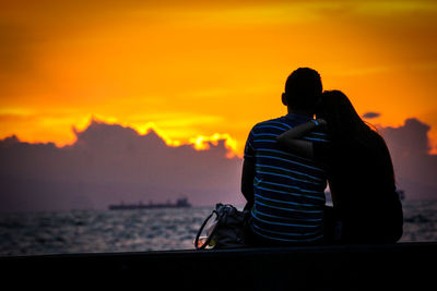 Rear view of silhouette couple against orange sunset sky