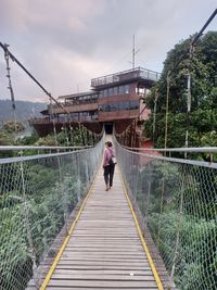 Rear view of woman walking on footbridge against building