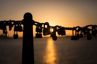 Close-up of padlocks hanging on chain against sea during sunset