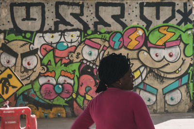 Rear view of woman against graffiti wall