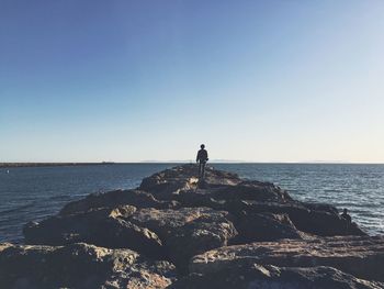 Rear view of man standing on beach against clear sky