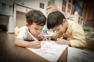 Siblings painting while lying on floor at home