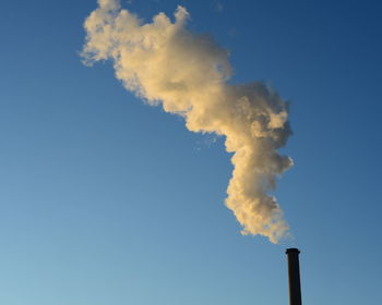 Low angle view of smoke emitting from chimney against blue sky