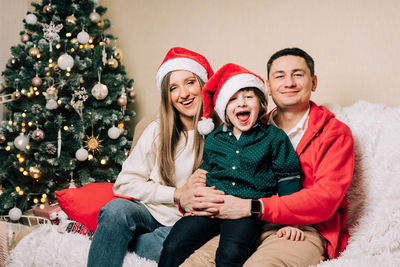 Portrait of cheerful parent and son sitting on sofa