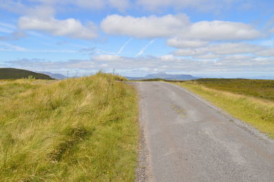 Empty road amidst field against sky