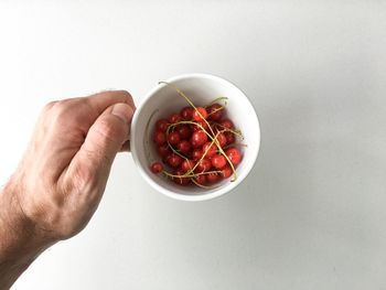 Cropped image of hand holding fruit over white background