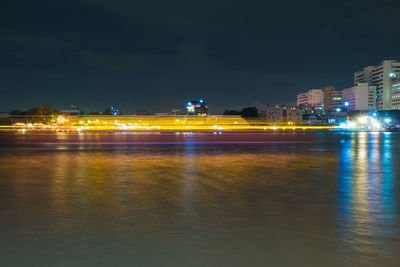 Illuminated city by river against sky at night