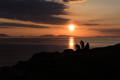 Silhouette people photographing on cliff against sky during sunset