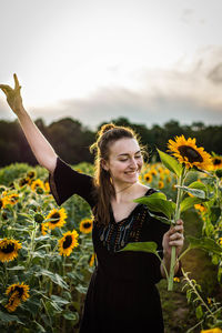 Smiling woman standing amidst sunflowers against sky