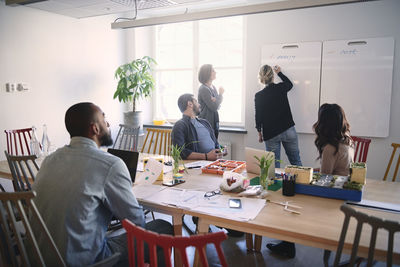 Female engineer explaining colleagues over whiteboard during meeting in office