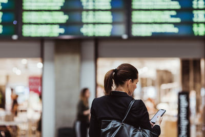 Rear view of female entrepreneur using smart phone while waiting at railroad station