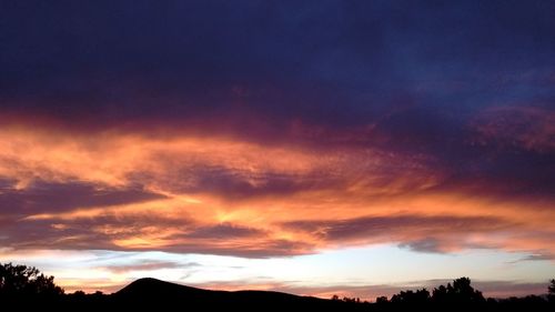 Silhouette trees against dramatic sky during sunset