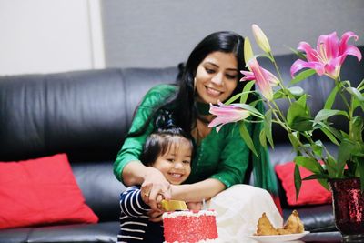 Smiling mother and boy cutting cake on table at home