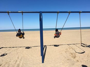 Children playing on swing at beach against sky