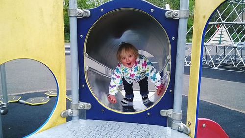 Portrait of happy girl playing on slide in playground