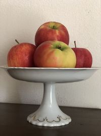 Close-up of apples in bowl on table against wall