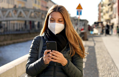 Woman wearing mask using phone on street