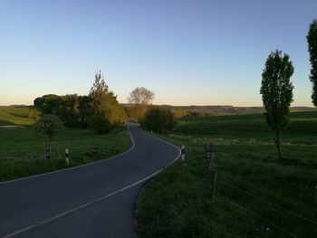 Road amidst field against clear sky