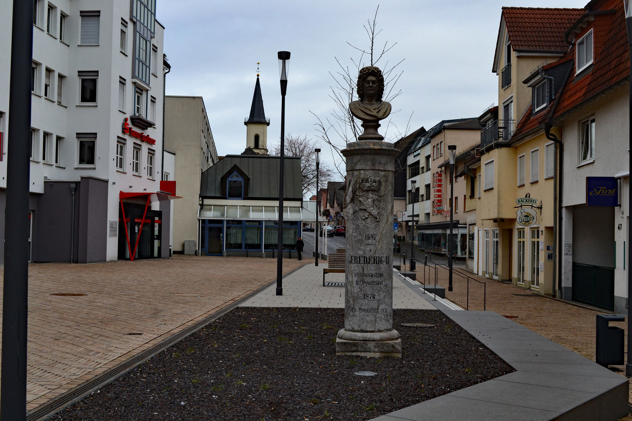 STATUE AMIDST STREET AND BUILDINGS AGAINST SKY