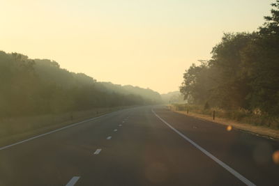 Road by trees against sky during sunset