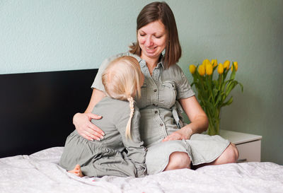 Smiling pregnant woman with her little daughter are talking and spending time together at home.