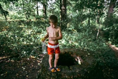 Full length of shirtless boy standing in forest