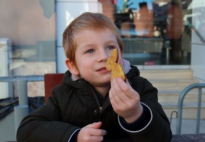 The boy holds a cookie in his hand and looks into the distance with a smile. happy five year old boy