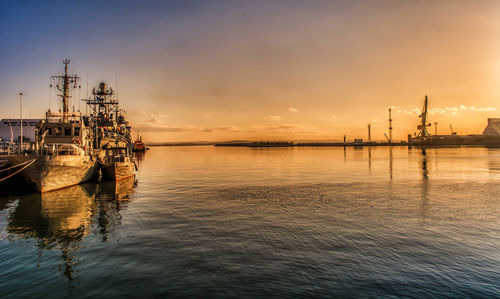 Boats moored in sea against sky during sunset