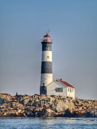 Lighthouse by sea against clear sky
