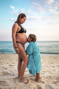 5 years old kid kissing the belly of his pregnant mother, at the beach