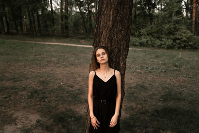Portrait of young woman standing against tree trunk in forest