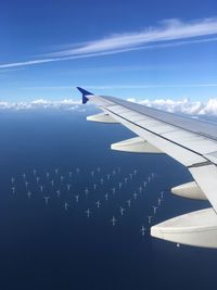 Airplane flying in sky above sea with wind turbines