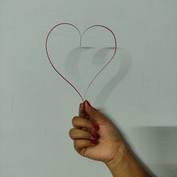 Close-up of hand holding heart shape against white wall