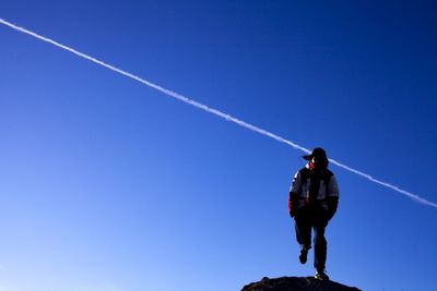 Low angle view of man standing on mountain against clear blue sky