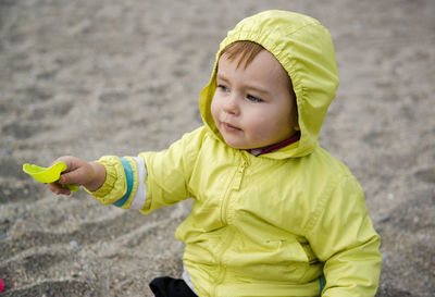 Close-up of cute baby girl holding shovel while sitting on sand at beach