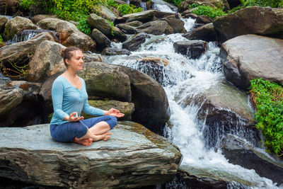 Woman meditating while sitting on rock