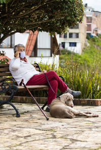 Full length of senior wearing mask with dog sitting outdoors