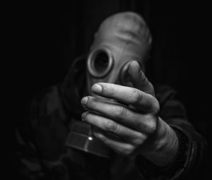 Close-up of man holding gas mask against black background