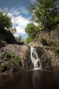 Scenic view of waterfall in forest against sky