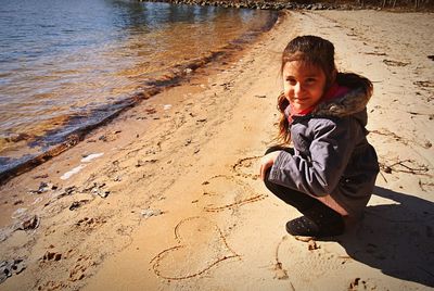 Portrait of cute girl crouching with heart shapes on sand at beach